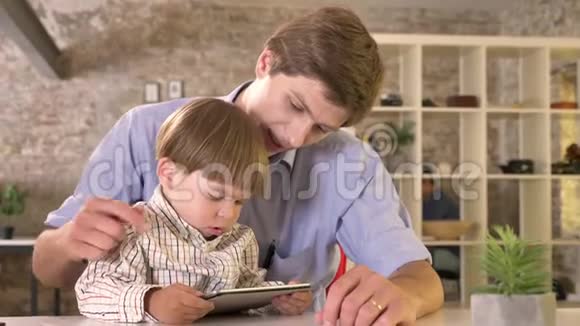 小男孩被他的父亲惹恼了他把爸爸的手从平板电脑移开坐在现代的办公室里视频的预览图