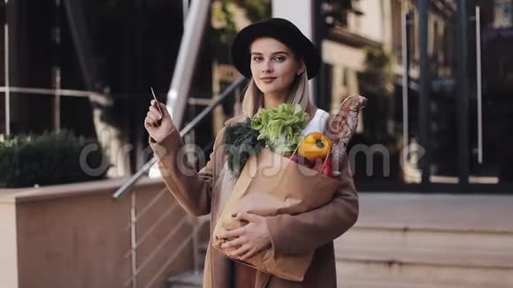 年轻漂亮的女人穿着时尚的外套站在街上拿着信用卡和产品包女孩视频的预览图