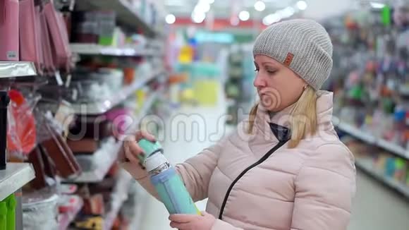 一位戴着帽子和羽绒服的中年妇女在超市里选择了一个热水瓶视频的预览图