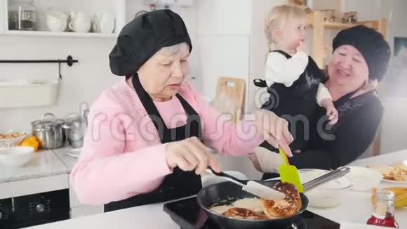 一位老妇人在厨房里做煎饼另一位老妇人手里拿着一个小女孩视频的预览图