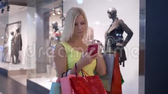 时尚购物迷人的女孩在逛商场的季节使用智能手机在网上商店购物视频的预览图