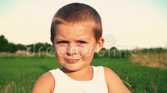 四岁的男孩穿着一件白色的t恤害羞地微笑着走进相机垂下眼睛一个小可爱的孩子的肖像视频的预览图