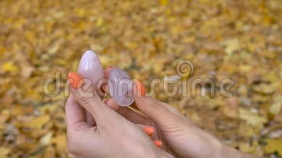 女性双手用橙色指甲手里拿着两个由粉红色石英和透明紫紫水晶制成的蛋黄蛋视频的预览图