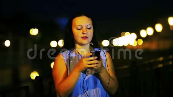 水边的年轻女子带着耳机听音乐在夜空的背景下唱歌视频的预览图