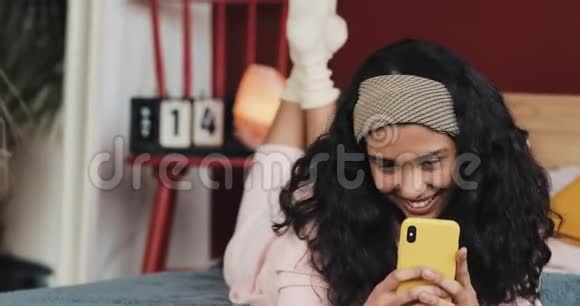 快乐的年轻女孩在家里用电话躺在床上发短信聊天在线交流视频的预览图