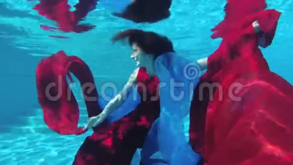 一个美丽的女孩穿着红裙子手拿红蓝相间的布在水下游泳跳舞看着镜头视频的预览图