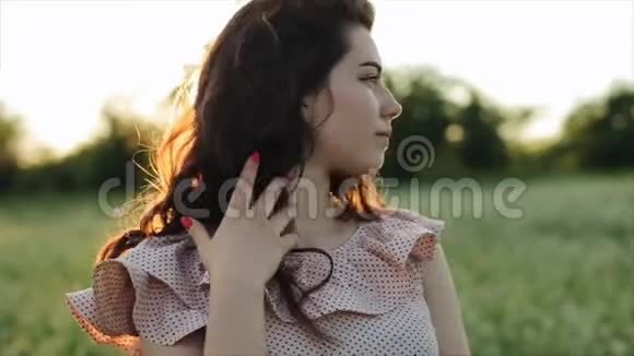 美丽的年轻无忧无虑的女孩长长的卷发笼罩着花麦田的景观背景夕阳西下视频的预览图