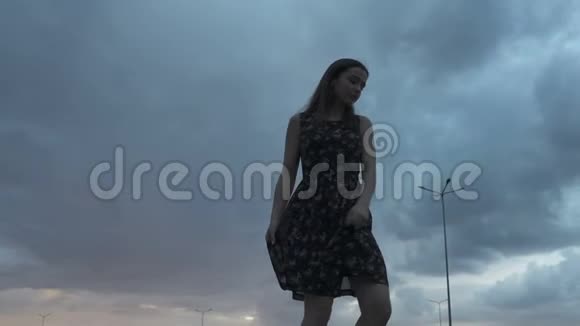 穿着夏装的年轻黑发女郎在乌云的天空下转身视频的预览图