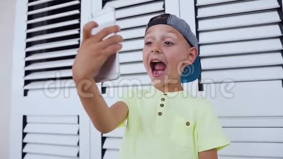 有趣的可爱男孩张开嘴在家里的智能手机上做自拍照片在白色背景上孤立儿童视频的预览图