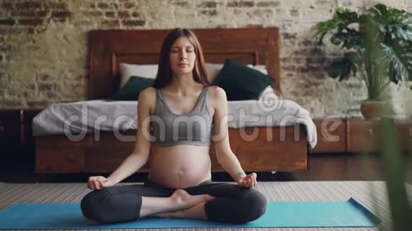 漂亮的黑发孕妇在地板上的垫子上放松双手练习哈他瑜伽视频的预览图