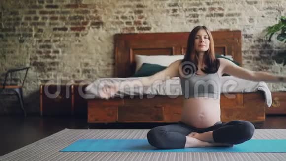 漂亮的孕妇正在做瑜伽坐在莲花的位置卧室的地板上明亮的垫子上女孩在举手视频的预览图