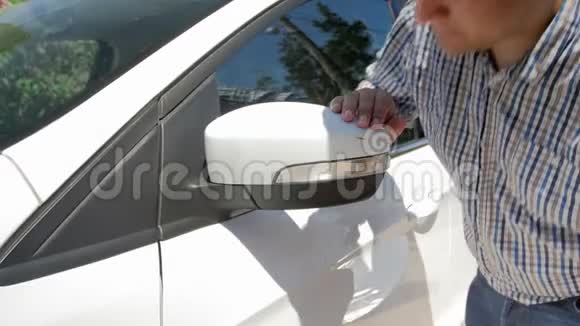 4k录像显示一名男子试图清除汽车侧镜上的油漆划痕视频的预览图