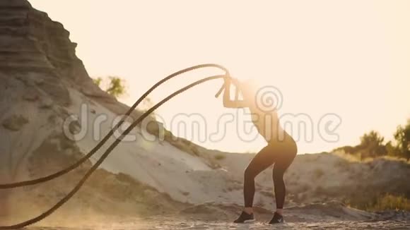 美丽的女孩运动员在沙地上站着用绳子在阳光下站在沙滩上做运动视频的预览图