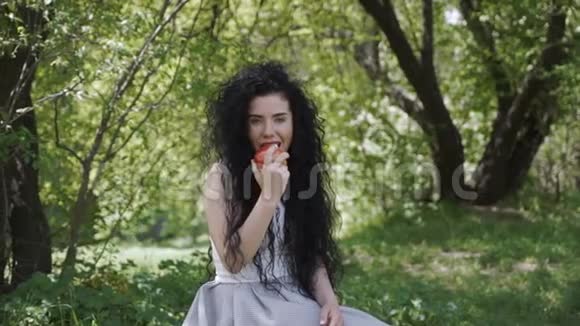 美丽的女人坐在夏天的花园里吃新鲜的苹果视频的预览图