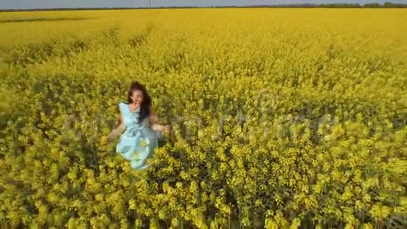 美丽的黑发女子穿着蓝色连衣裙站在田野上的黄花间视频的预览图