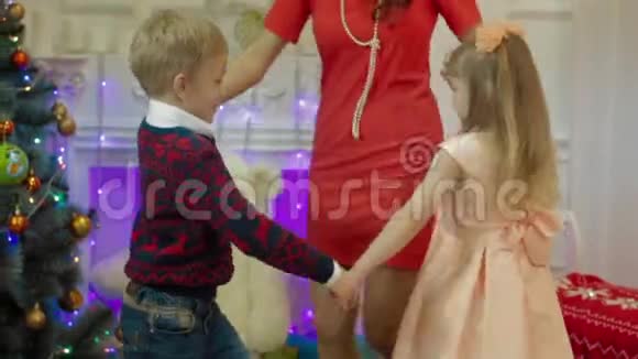 快乐的母亲和孩子们在圣诞树的背景下跳舞视频的预览图