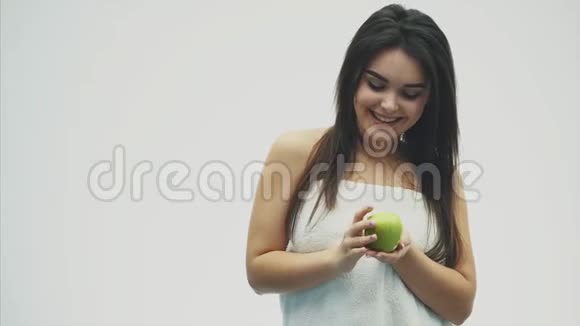 白色背景上一个年轻迷人的女孩的肖像指导和检查绿色苹果孤立于白色视频的预览图