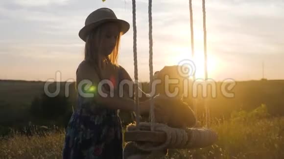 在日落时戴帽子的快乐有趣的女孩正在玩一只泰迪熊在绳子上摆动孩子在户外玩大自然视频的预览图