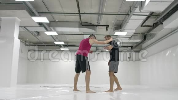 在一间白色的房间里两个男摔跤手在扔垫子抓住一个抓斗把自己扔出去视频的预览图