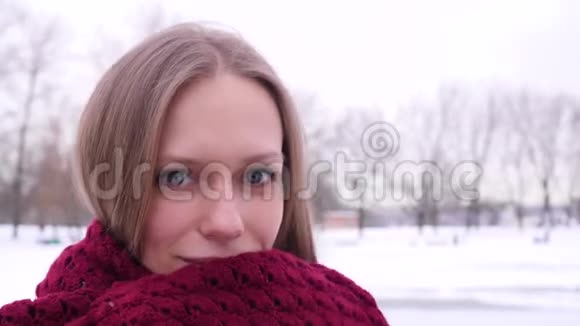 冬天城市公园里一个年轻的蓝眼睛漂亮微笑的女人的肖像她看着摄像机把自己包起来视频的预览图