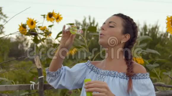 动作慢拿着硬币的美女在生长着的向日葵的背景运行肥皂泡视频的预览图