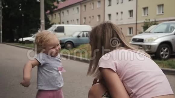 蓝眼睛的小卷发女孩正在街上和她的母亲挥手视频的预览图