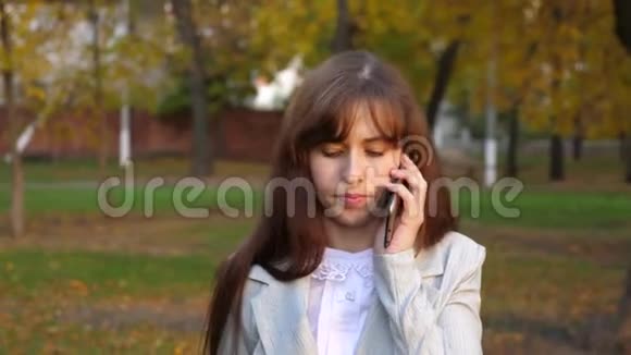 漂亮的女人在智能手机上说话微笑着女孩正在用手机说话在城市公园散步视频的预览图
