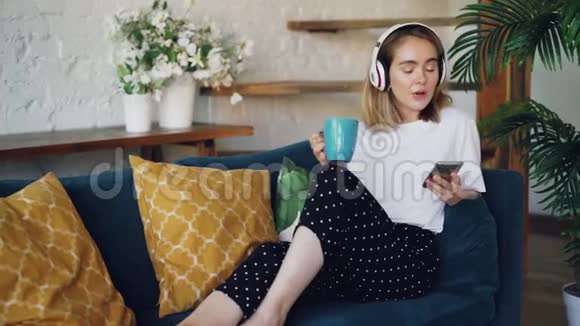 现代年轻女性正在家里舒适的沙发上休息里面有智能手机茶和耳机女孩在听视频的预览图