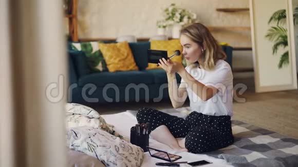 有魅力的金发年轻女人正在家里用刷子和化妆品在床上化妆现代视频的预览图