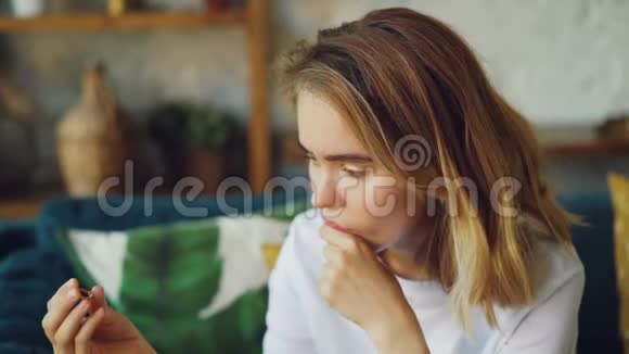 一幅不幸的女人看着订婚戒指摸着她的脸独自坐在家里叹息的肖像婚姻视频的预览图