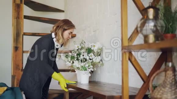 戴着橡胶防护手套的金发主妇正在家里擦桌子做家务耳机楼梯和视频的预览图