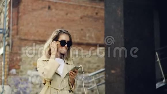 漂亮的女孩正在用智能手机听音乐在街上跳舞享受音乐视频的预览图