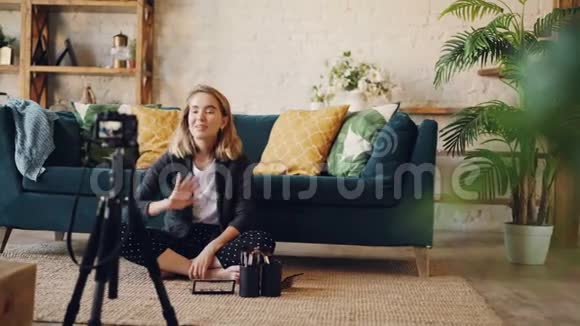 受欢迎的女性博客作者正在录制关于化妆和美容的视频坐在家里的地板上用三脚架上使用相机视频的预览图