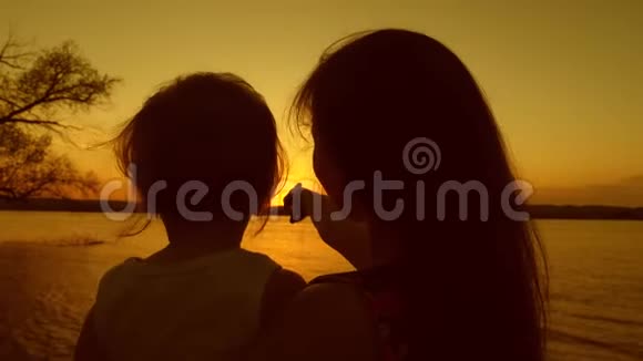 妈妈和女儿欣赏美丽的日落日落时一位年轻母亲手中的孩子在金色的阳光下视频的预览图