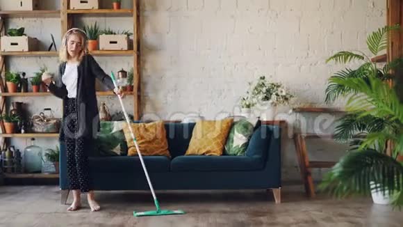 有创意的女孩在漂亮的房子里和漂亮的家具和植物一起做家务用拖把唱歌跳舞乐趣视频的预览图