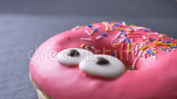 特写上景的美味的粉红色甜甜圈与五颜六色的薯片和眼睛慢慢旋转在灰色的桌子背景视频的预览图