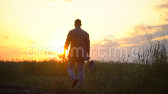 农夫在日落或日出时穿过田野带着一棵树苗和铲子理念在花园里工作视频的预览图