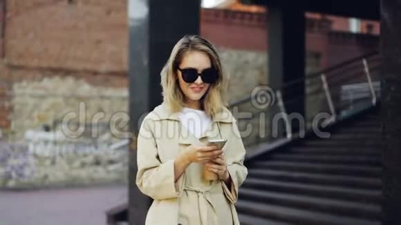 优雅的年轻女士走在街上使用智能手机喝着咖啡享受着美丽的散步视频的预览图