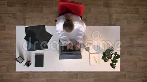 年轻的女医生坐在桌子旁用手提电脑打字检查x光扫描上面的照片视频的预览图