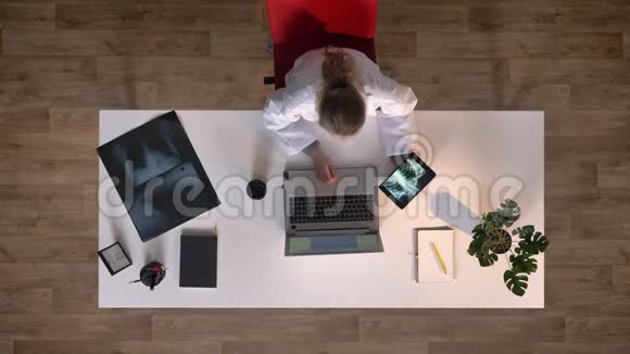 年轻的女医生拿着X光图像的平板电脑在笔记本电脑上打字顶级医学概念视频的预览图