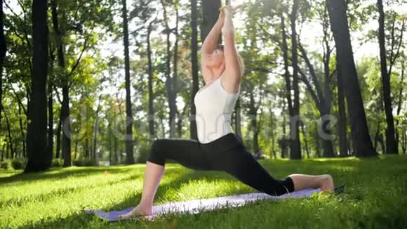 在公园草地上练习瑜伽的40年代女性慢动作视频成年女士在森林里的垫子上做健身运动视频的预览图