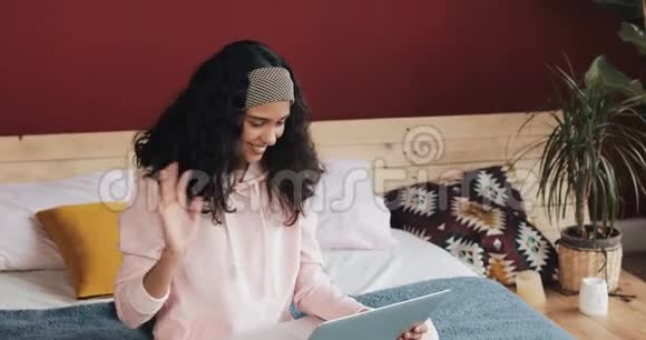 年轻漂亮的女人坐在舒适的家里的床上在笔记本电脑上和一个视频电话上的人愉快地聊天视频的预览图