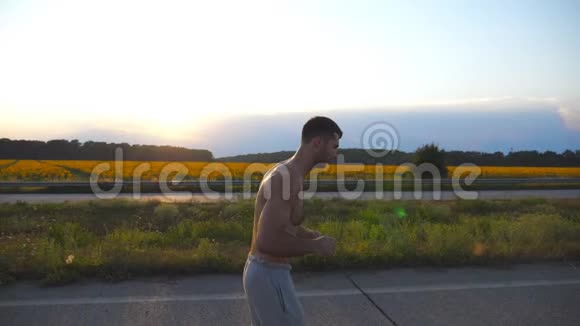 日落时分年轻的肌肉男在乡间小路上慢跑马拉松长跑户外男子慢跑训练概况运动员视频的预览图