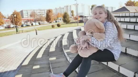 年轻的金发女孩带着玩具熊在户外视频的预览图