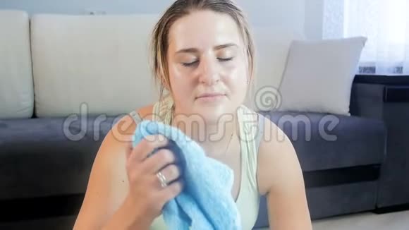 疲惫的年轻女子坐在健身垫上用毛巾擦着额头上的汗视频的预览图