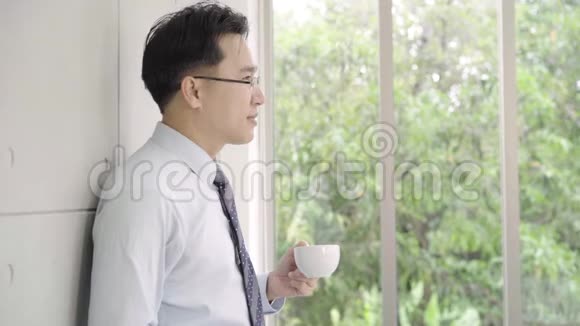 慢动作成熟的亚洲商人喝着咖啡从办公楼向窗外眺望城市的天际线视频的预览图