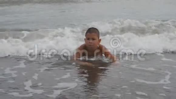 孩子躺在海浪中的沙岸上男孩在海滩上划沙孩子洗了海浪视频的预览图