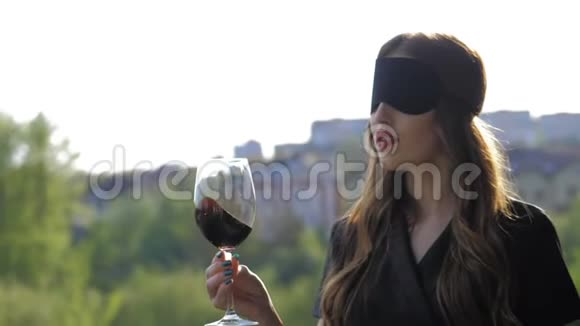 戴着黑脸面具的性感女孩在大自然背景下喝红酒视频的预览图