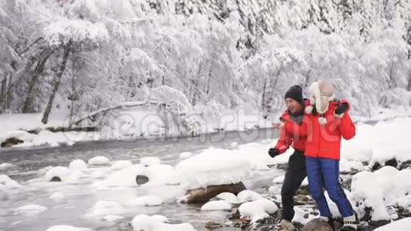一对相爱的夫妇在冬天的森林里向流过美丽风景的溪流扔石头视频的预览图