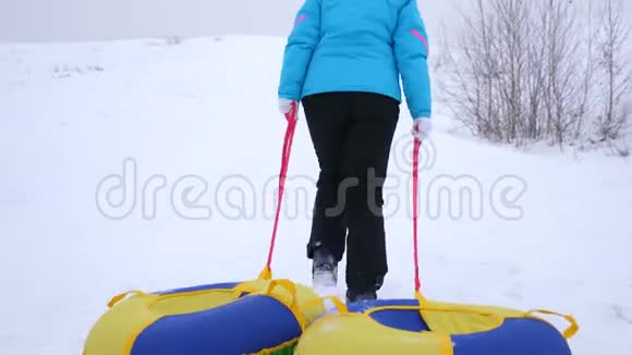 女孩爬上雪山拉雪橇和一个充气雪管在冬季公园休息过圣诞节视频的预览图